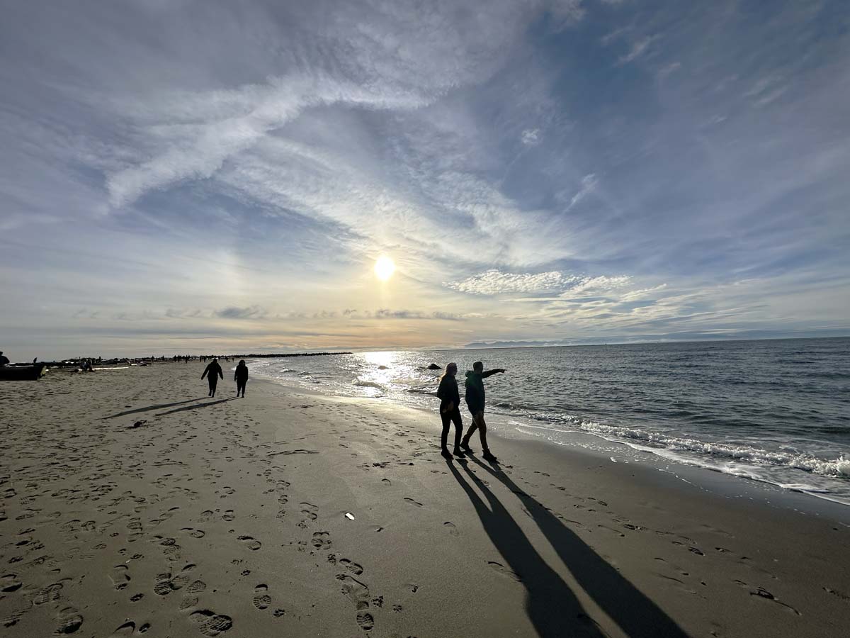 People walking along the shoreline at Wreck Beach during sunset.