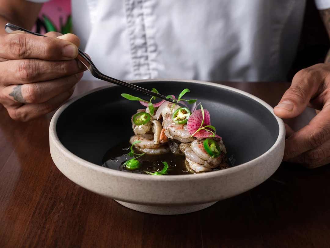 Shrimp aguachile with jalapeño and radish in black bowl.