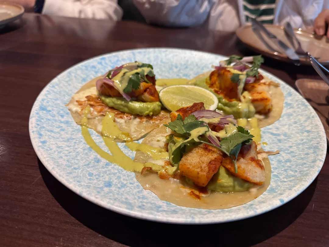 Three fish tacos topped with guacamole, onion, and cilantro.