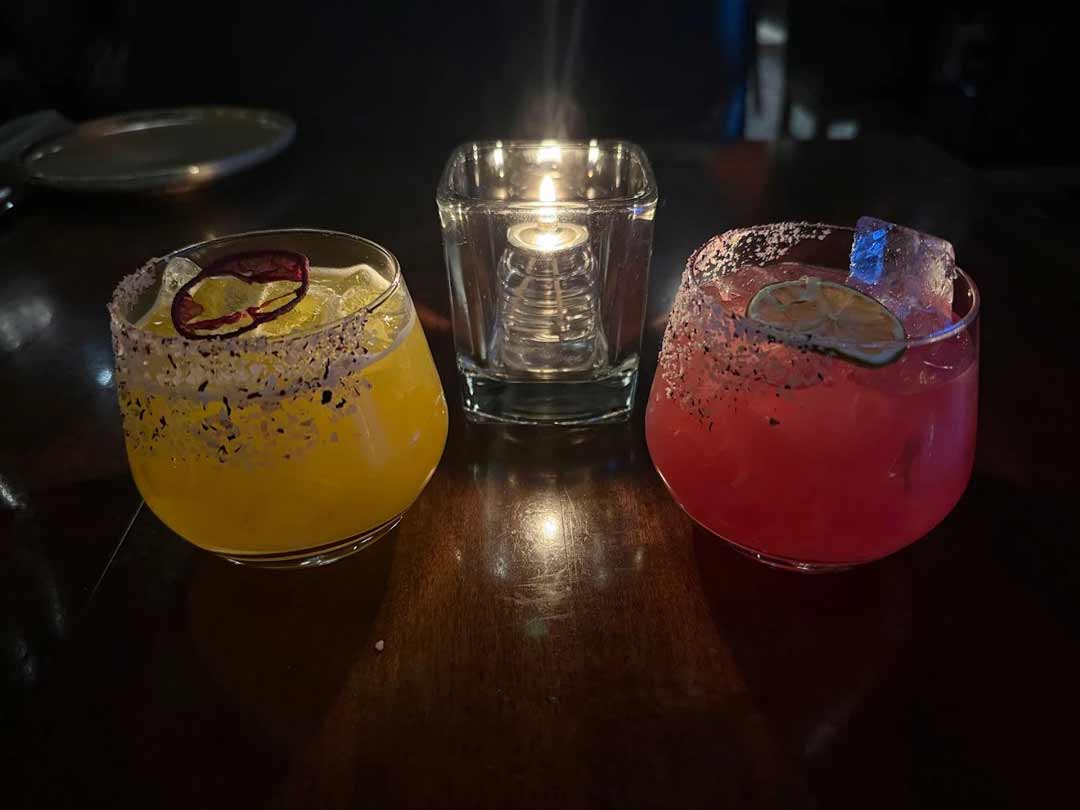 Two colorful cocktails with salt rims, lit by a candle.