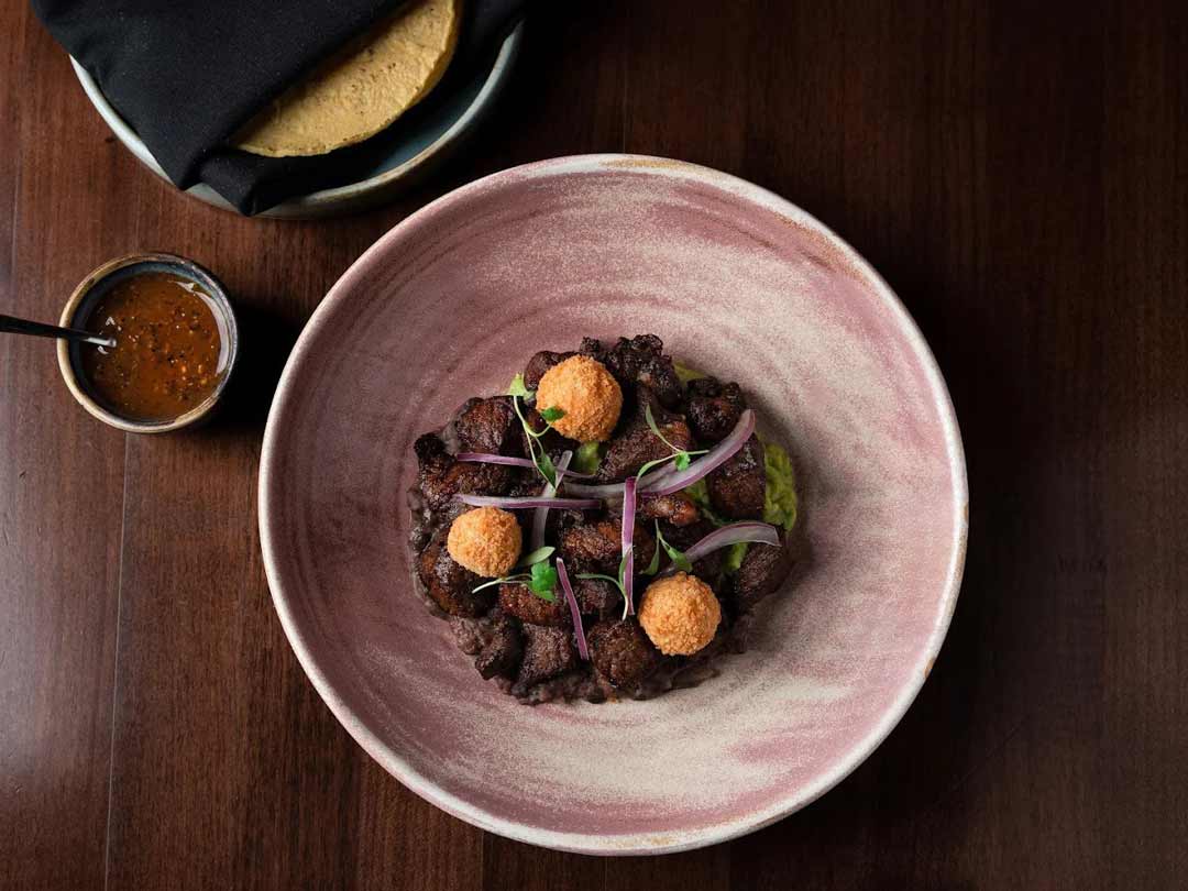 Plated Mexican dish with grilled meat, sauce, and garnishes.