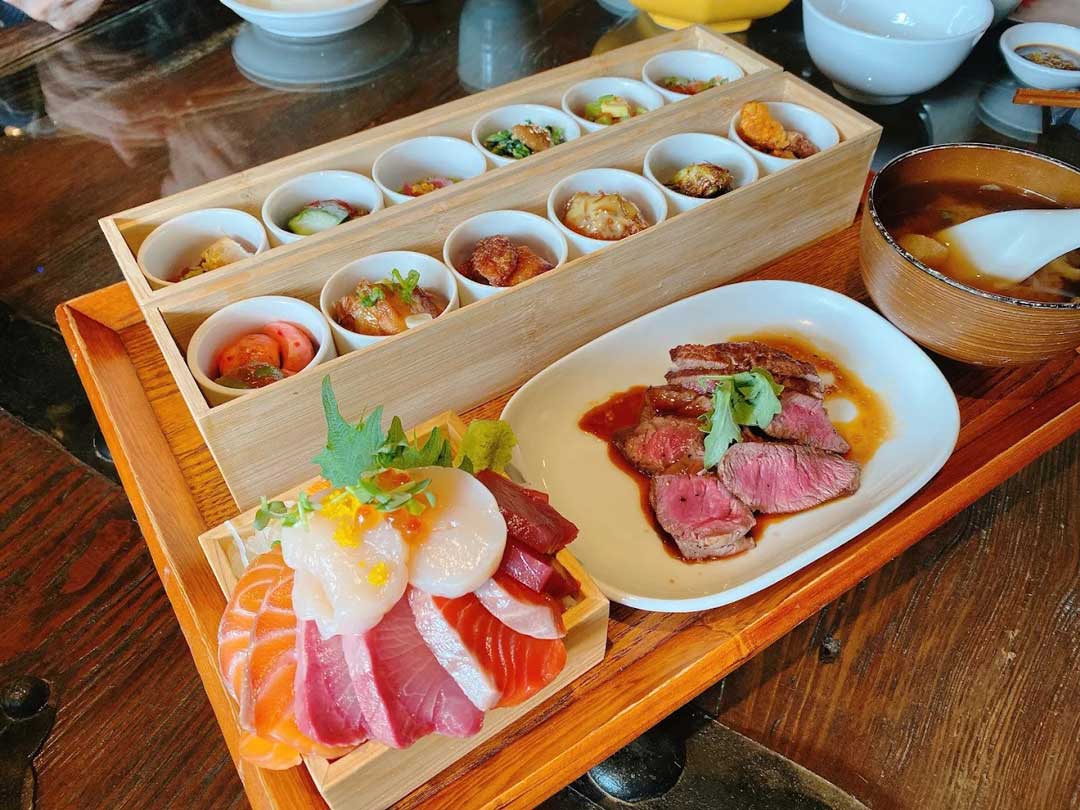 Japanese lunch set with sashimi, steak, and side dishes.