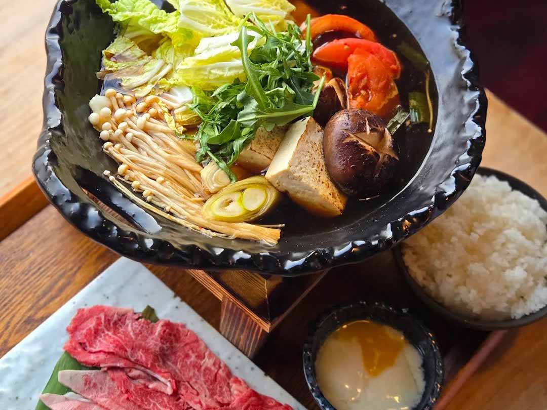 Sukiyaki hot pot with vegetables, beef slices, and rice.
