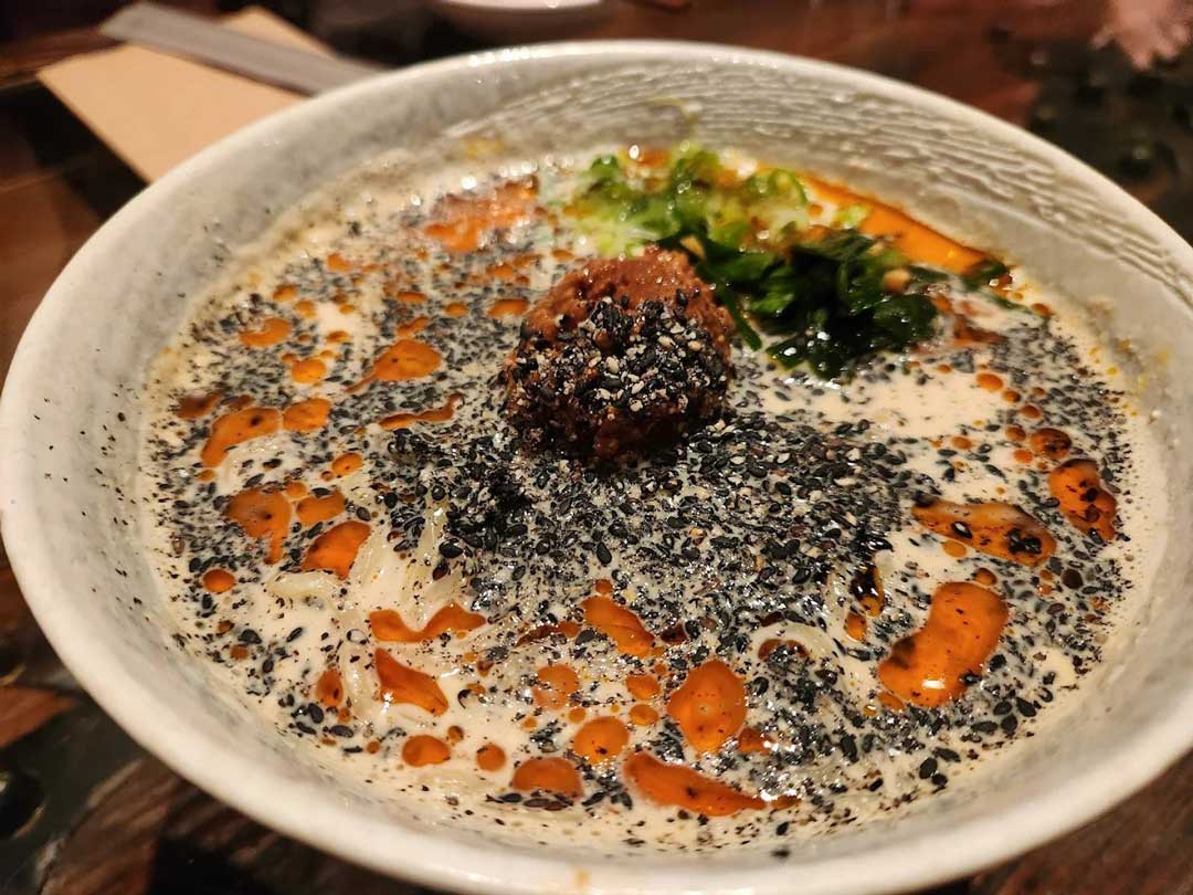 Bowl of rich ramen topped with sesame seeds and chili oil.